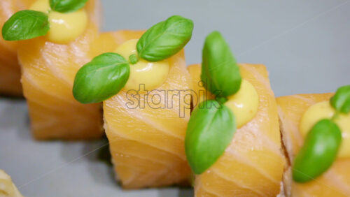 A plated dish of salmon sushi, neatly arranged with green garnish on top with soy sauce in a small bowl, plus wasabi and pickled ginger on the side