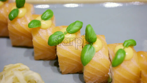 A plated dish of salmon sushi, neatly arranged with green garnish on top with soy sauce in a small bowl, plus wasabi and pickled ginger on the side