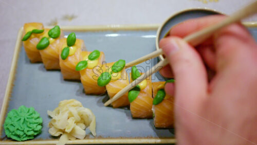 Chopsticks pick up a piece of sushi and dip it into soy sauce