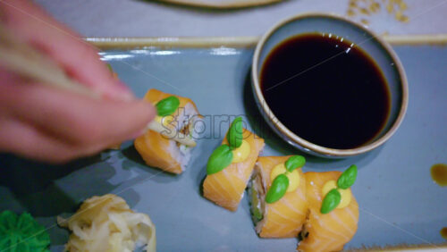Chopsticks pick up a piece of sushi and dip it into soy sauce