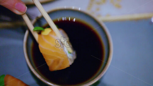 Close up pf chopsticks dipping a piece of sushi into soy sauce