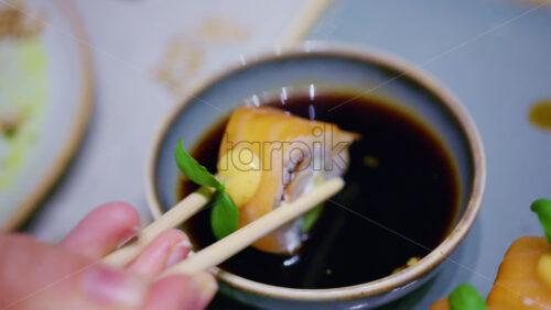Close up pf chopsticks dipping a piece of sushi into soy sauce