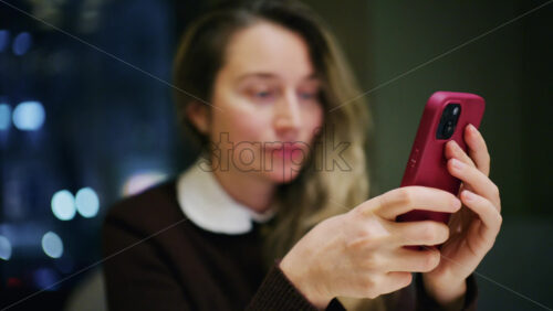 A woman indoors at night, softly lit, looking at her phone with a slight smile