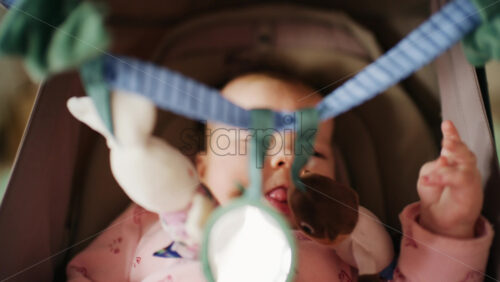 Infant lying on back under a soft baby play gym, looking up at hanging plush toys and a small mirror