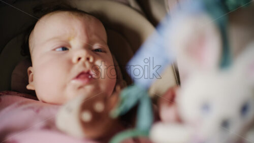 Infant lying on back under a soft baby play gym, looking up at hanging plush toys and a small mirror