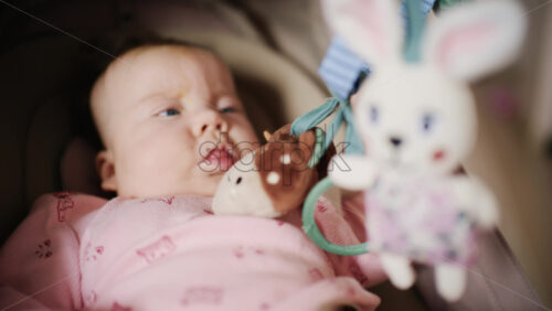 Infant lying on back under a soft baby play gym, looking up at hanging plush toys and a small mirror