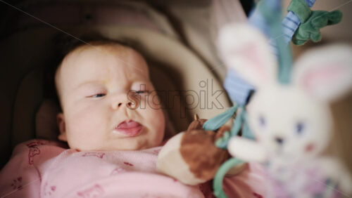 Infant lying on back under a soft baby play gym, looking up at hanging plush toys and a small mirror