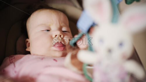 Infant lying on back under a soft baby play gym, looking up at hanging plush toys and a small mirror