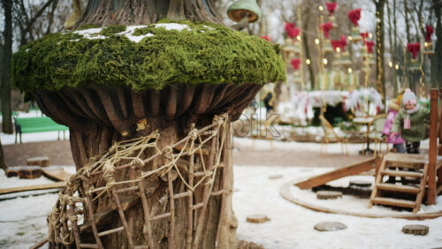 Winter park scene with children playing near a whimsical treehouse style structure decorated with moss and fairy tale elements
