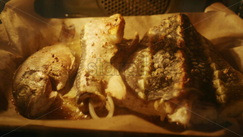 Fresh fish pieces roasting in the oven on a tray, golden surface and steam visible.