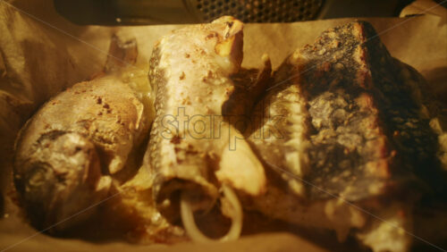 Fresh fish pieces roasting in the oven on a tray, golden surface and steam visible.