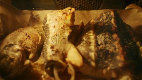 Fresh fish pieces roasting in the oven on a tray, golden surface and steam visible.