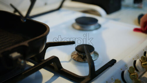 Close up of a woman cleaning a domestic gas stove with a cast iron pan placed on the burner