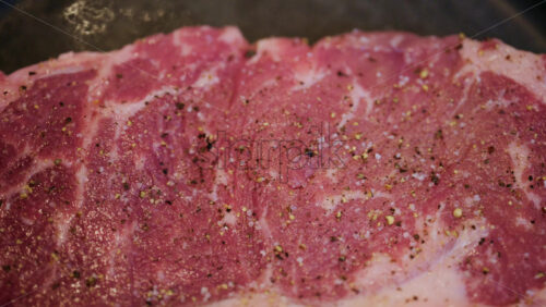 Close up of a raw beef steak seasoned with salt and black pepper in a pan