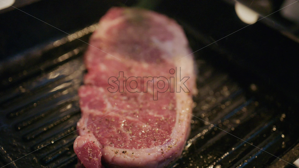 Hand placing a seasoned beef steak onto a ridged grill pan. Beginning the grilling process indoors