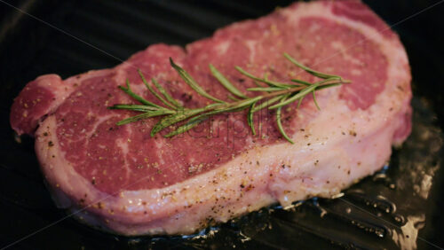 Close up of steak cooking on a grill pan topped with fresh rosemary