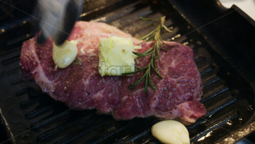 Close up of butter melting over a steak with garlic and rosemary in a hot grill pan