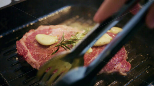 Close up of butter melting over a steak with garlic and rosemary in a hot grill pan
