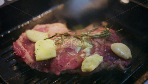 Close up of butter melting over a steak with garlic and rosemary in a hot grill pan