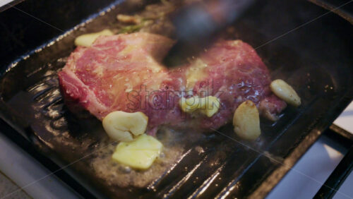 Close up of butter melting over a steak with garlic and rosemary in a hot grill pan