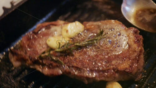 Cooked steak browning in a grill pan while being basted with melted butter and herbs