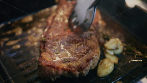 Cooked steak browning in a grill pan while being basted with melted butter and herbs