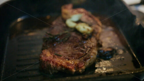 Close up of a juicy steak sizzling in a grill pan while being pressed with a spatula