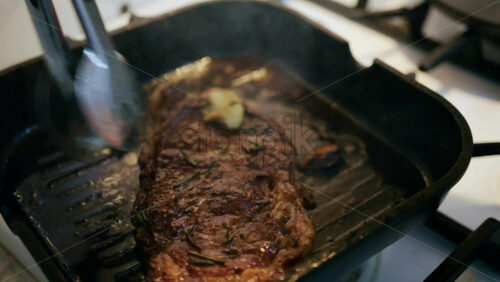 Close up of a juicy steak sizzling in a grill pan while being pressed with a spatula