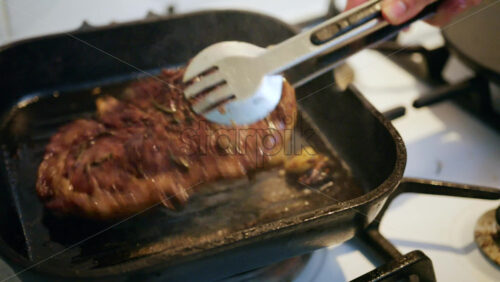 Close up of a juicy steak sizzling in a grill pan while being pressed with a spatula
