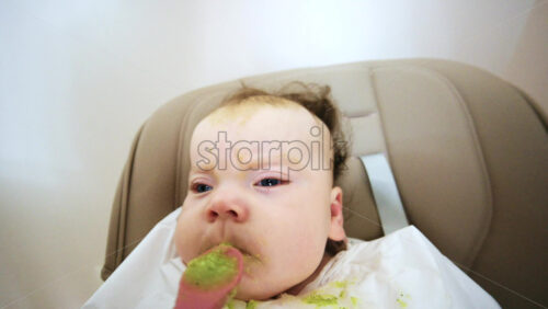 Close up of a baby eating green vegetable puree from a spoon while sitting in a high chair