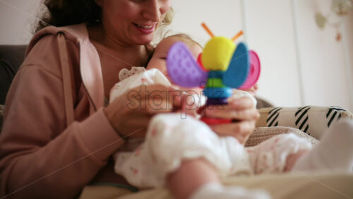 Smiling mother playing with her baby using a colorful toy at home
