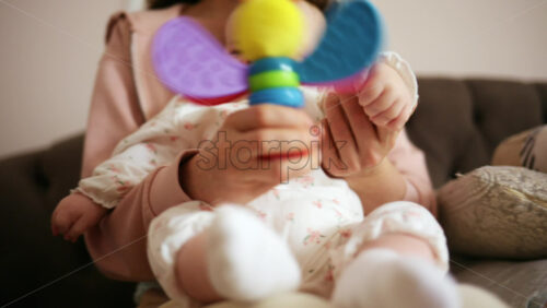 Baby holding a bright, colorful toy while sitting on a parent's lap