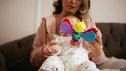 Smiling mother playing with her baby using a colorful toy at home