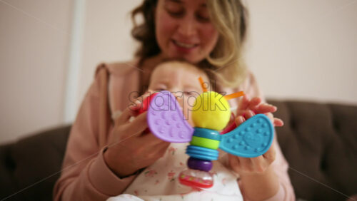 Baby holding a bright, colorful toy while sitting on a parent's lap