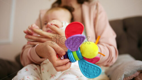 Smiling mother playing with her baby using a colorful toy at home