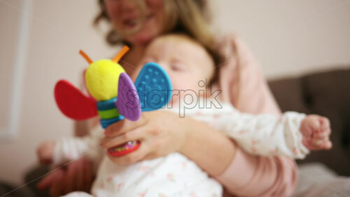 Smiling mother playing with her baby using a colorful toy at home