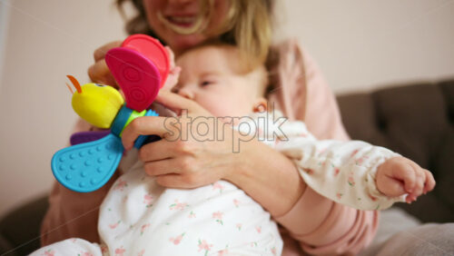 Smiling mother playing with her baby using a colorful toy at home