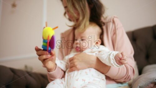 Smiling mother playing with her baby using a colorful toy at home