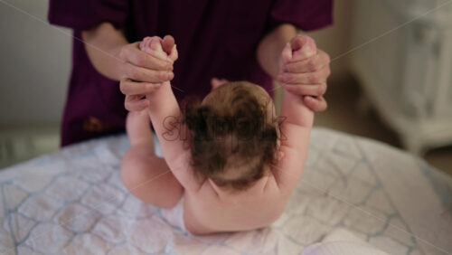 Adult holding a baby's hands to help them stand on a soft surface