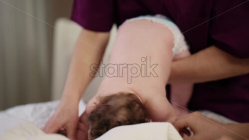 Baby lying on their tummy while an adult massages them and performs mobility exercises