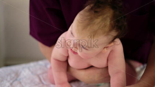 Baby sitting upright while being supported by an adult, showing effort and focus
