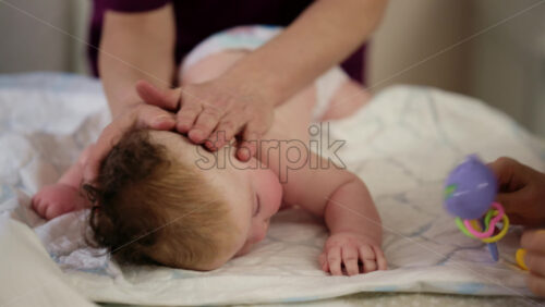 Woman trying to distract a crying baby lying on a blanket during massage with a toy