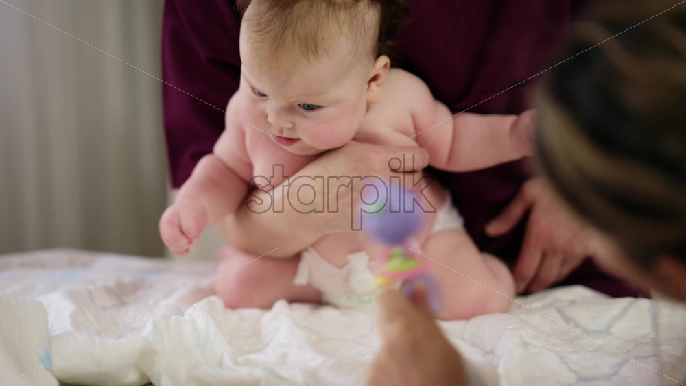 Woman trying to distract a crying baby lying on a blanket during massage with a toy