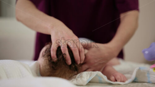 Woman trying to distract a crying baby lying on a blanket during massage with a toy