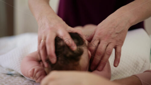 Woman trying to distract a crying baby lying on a blanket during massage with a toy