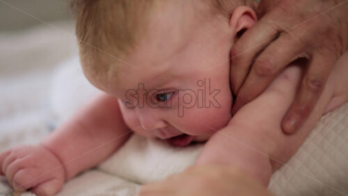 Woman trying to distract a crying baby lying on a blanket during massage with a toy