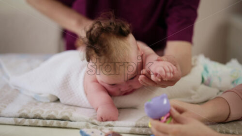 Woman trying to distract a crying baby lying on a blanket during massage with a toy