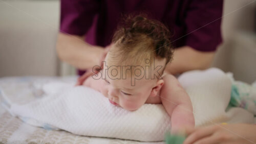 Woman trying to distract a crying baby lying on a blanket during massage with a toy