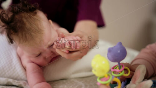 Woman trying to distract a crying baby lying on a blanket during massage with a toy
