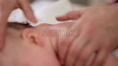 Woman trying to distract a crying baby lying on a blanket during massage with a toy